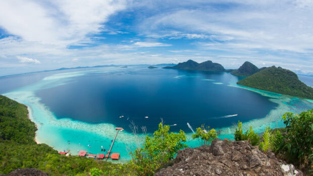 A panoramic ocean landscape with lush green islands and clear turquoise water viewed from a rocky cliff