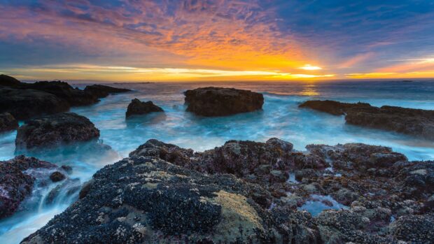 Rocky ocean landscape with vibrant sunset sky and misty waves