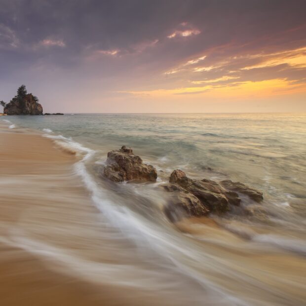 Ocean landscape with rocky shore and gentle waves under a cloudy sunset sky
