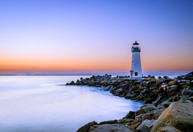 A peaceful ocean landscape with a lighthouse standing on rocky shore during sunset