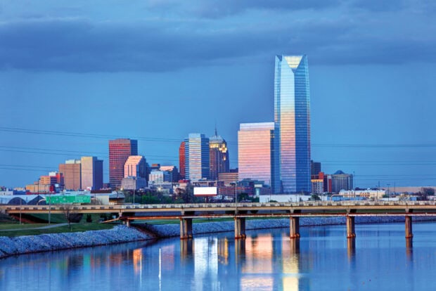 A clear view of Oklahoma City skyline with tall buildings reflecting on calm water at dusk