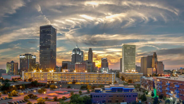 Oklahoma City skyline features tall buildings under a dramatic sunset sky with glowing city lights