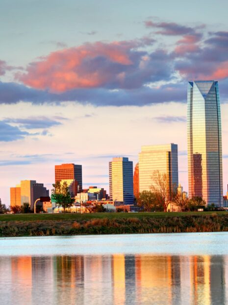 The Oklahoma City skyline reflecting on water during sunset with colorful clouds in the sky