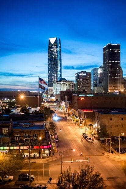 Evening view of Oklahoma City skyline with illuminated buildings and flags