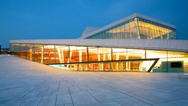 Modern architecture of Oslo Opera House with illuminated glass facade at dusk