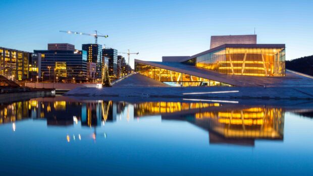 Modern architecture in Oslo reflecting on calm water at dusk with city skyline in the background
