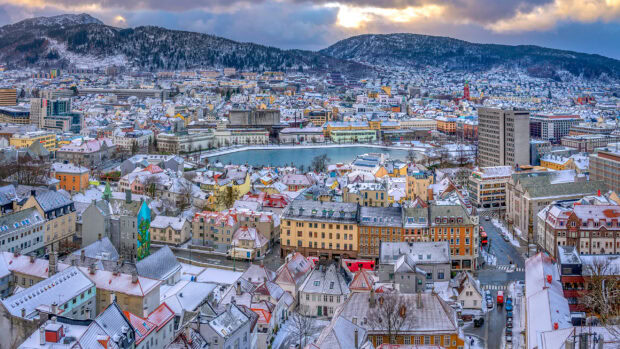 Snow covered rooftops and lake in Oslo city with surrounding hills under cloudy sky