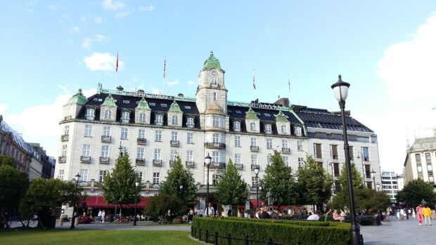 The grand building in Oslo city center surrounded by trees and people on a sunny day
