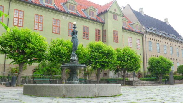 Statue fountain with green trees and old buildings in Oslo city center