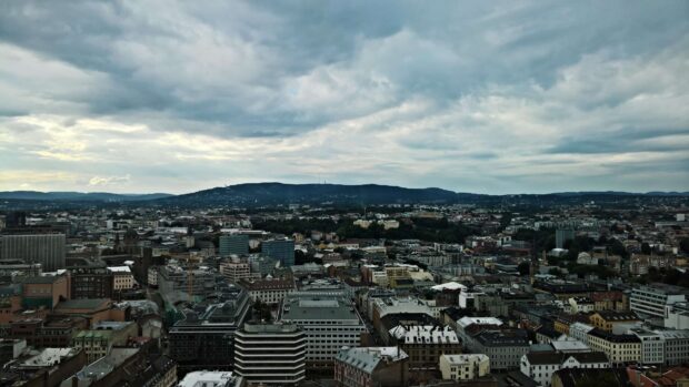 A panoramic view of Oslo cityscape with hills in the background under a cloudy sky