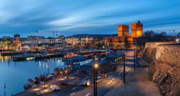 Evening cityscape of Oslo with harbor and illuminated buildings under a cloudy sky
