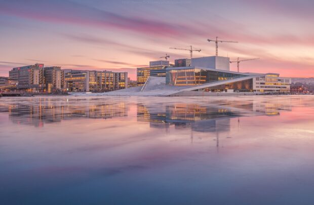 Modern architecture in Oslo city under colorful sunset sky reflecting on calm water