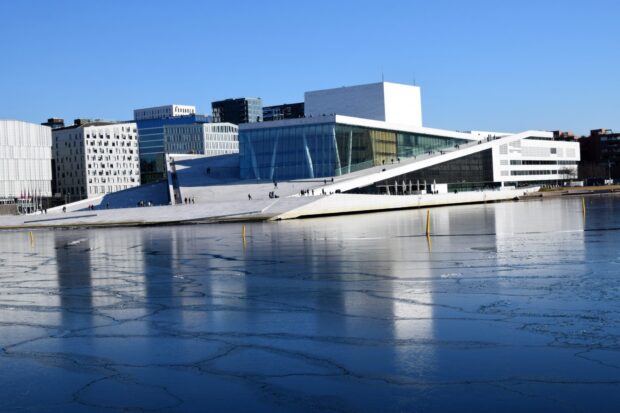 Modern architecture in Oslo reflecting on icy water with a clear blue sky