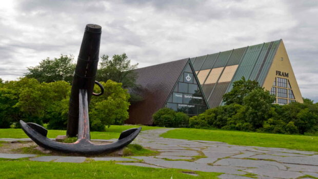 A large anchor sculpture in front of the Fram Museum in Oslo surrounded by green grass and trees
