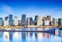 Modern Oslo skyline with skyscrapers reflecting on calm water under blue sky