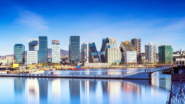 Modern Oslo skyline with skyscrapers reflecting on calm water under blue sky