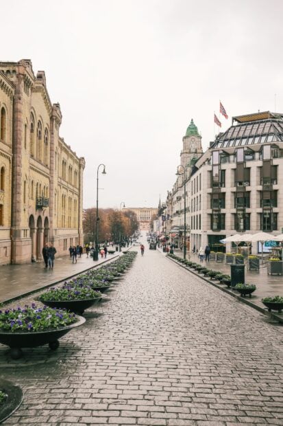 Historic Oslo street with flowers and pedestrians on a cloudy day