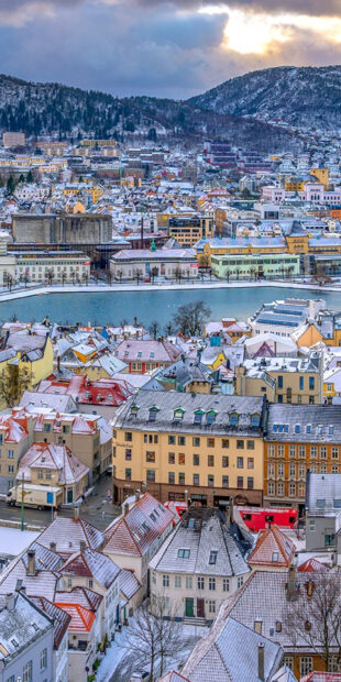 Snow covered roofs and buildings in Oslo cityscape under a cloudy sky