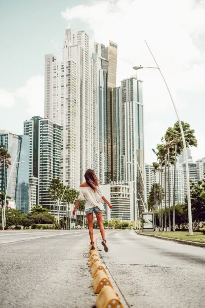 A woman walking on the road divider in Panama City with tall modern buildings in the background