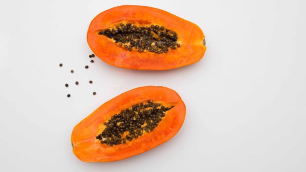 Fresh papaya cut in half with black seeds spilling on a white surface