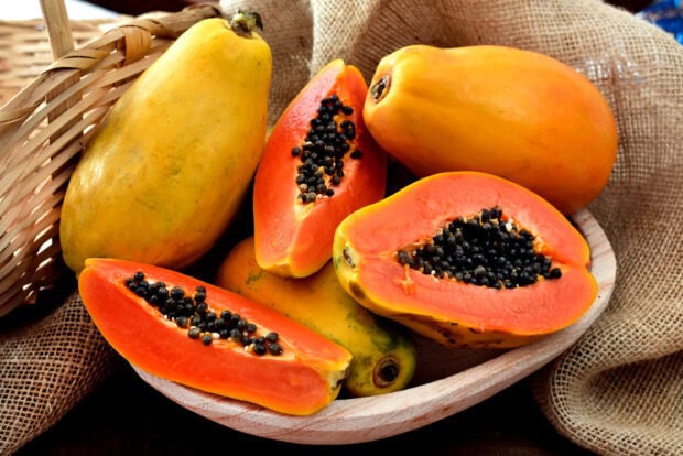 Fresh papaya fruit cut open with black seeds in a wooden bowl on a rustic background