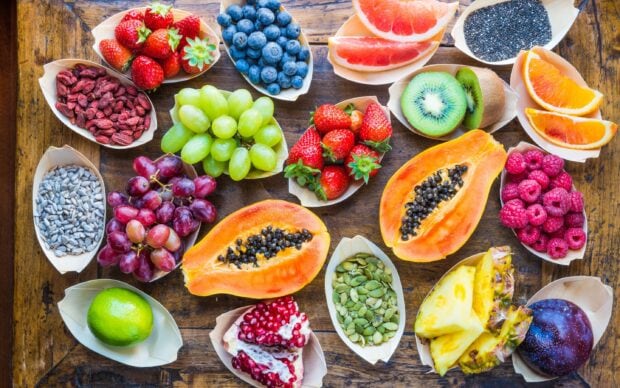 Fresh papaya surrounded by various colorful fruits on wooden table
