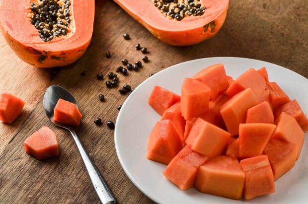 Fresh cut papaya pieces on a white plate with papaya seeds on a wooden surface
