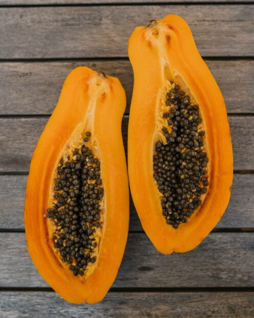 Fresh papaya cut in half with visible seeds on a wooden surface
