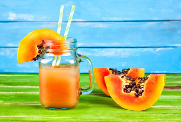 A glass of papaya juice with fresh papaya slices on a colorful wooden table