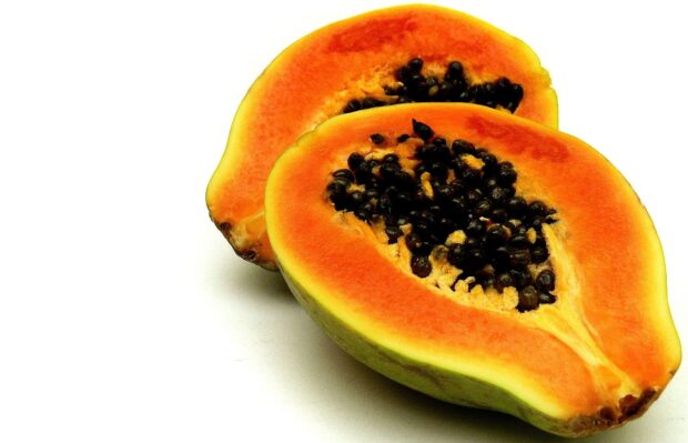 Fresh papaya with ripe orange flesh and black seeds cut in half on white background