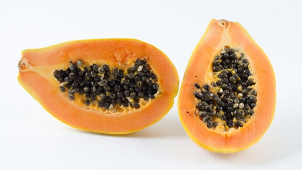 Fresh ripe papaya cut in half showing seeds and orange flesh on white background