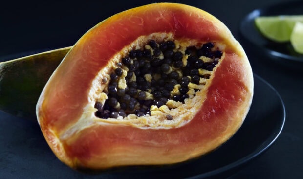 Half cut fresh papaya showing seeds and orange flesh on a black plate