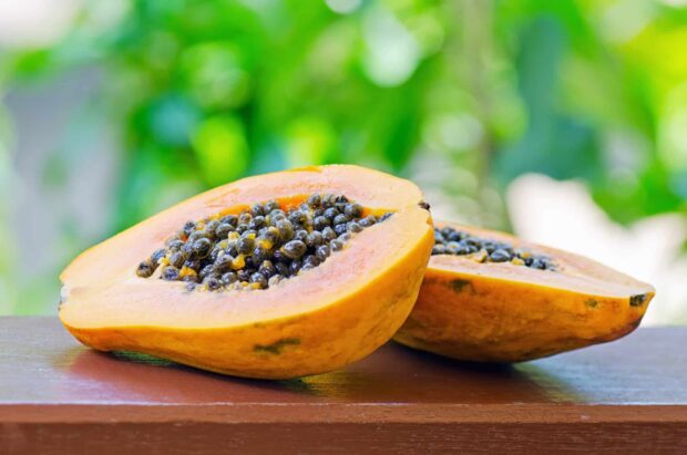 Fresh papaya cut open revealing ripe seeds on a wooden surface