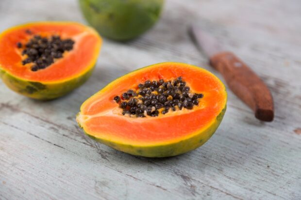 Fresh papaya fruit cut in half showing ripe seeds on a wooden surface
