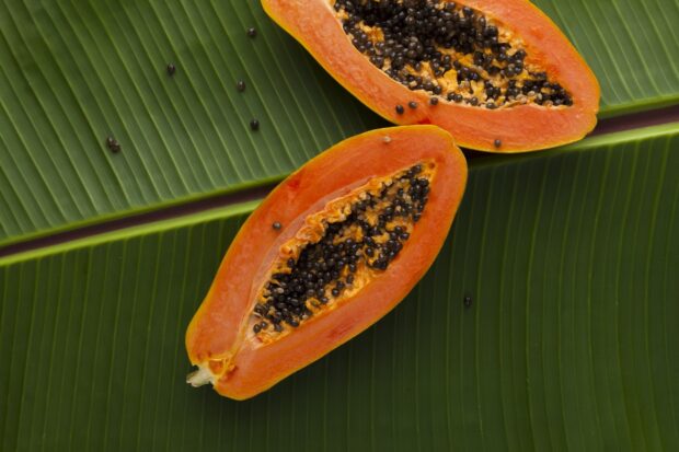 Fresh papaya fruit cut in half showing seeds on green banana leaves