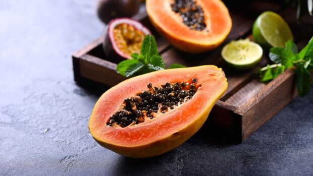 Fresh papaya fruit cut open with seeds visible on a dark surface