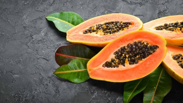 Fresh papaya with black seeds placed on green leaves on a textured surface