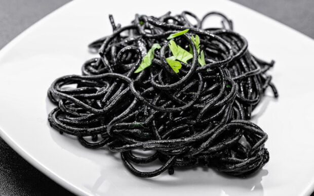 Black squid ink pasta garnished with fresh green herbs on a white plate