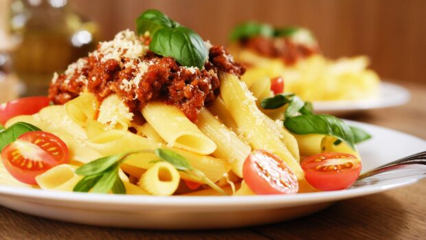 Delicious pasta dish with tomato sauce and fresh basil leaves on a white plate