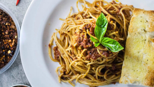 Spaghetti pasta served with meat sauce and basil leaf on a white plate with toasted bread