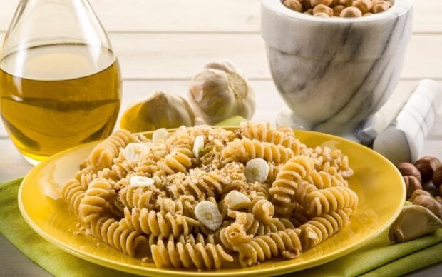 A plate of spiral pasta with garlic slices and crushed nuts on a yellow plate