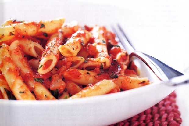 Close up of pasta with tomato sauce and herbs in a white bowl with a fork