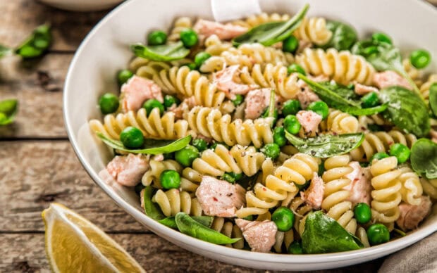 Fresh pasta with peas and salmon pieces in a bowl on wooden table