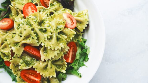 Green pesto pasta with cherry tomatoes and fresh greens in a white bowl