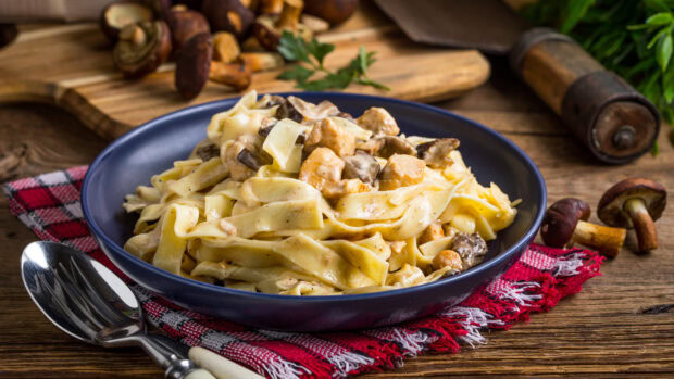 Creamy pasta with mushrooms and chicken served in a bowl on a wooden table