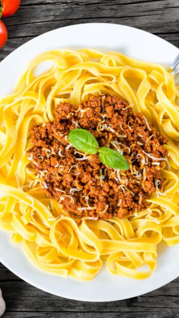 A plate of pasta topped with minced meat sauce and garnished with fresh basil leaves