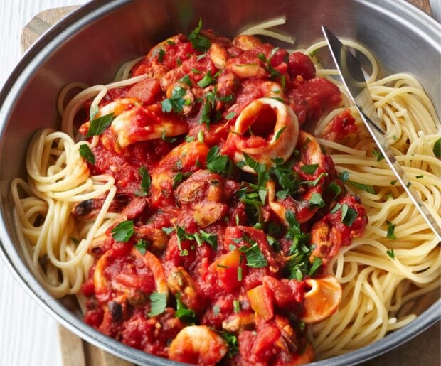 Spaghetti with tomato sauce and seafood garnished with fresh herbs in a metal pan
