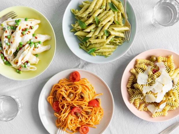 A variety of pasta dishes including penne with basil pesto and spaghetti with cherry tomatoes on a table
