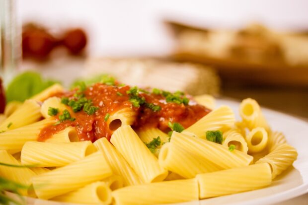 Close up of pasta with tomato sauce and chopped herbs on a plate
