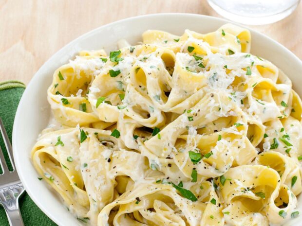 Creamy pasta with herbs and grated cheese on a white plate